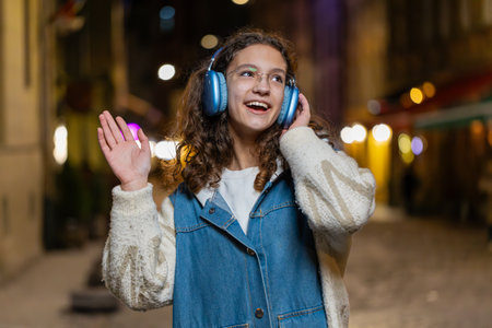 Happy relaxed lovely teenage girl in wireless headphones choosing listening favorite energetic disco...