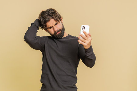 Young man using mobile cell phone typing browsing, loses becoming surprised sudden lottery results, bad fortune, loss, fail. Handsome guy male isolated on beige studio background.の写真素材