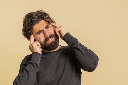 Bearded man in long sleeves rubbing temples to cure headache problem, suffering from tension,...
