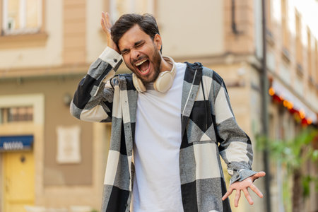 Young man screams yell shout from stress tension problems feels horror hopelessness fear panic surprise shock expresses gestures rage. Frustrated guy standing in urban city street.の写真素材