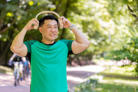 Happy young Japanese man put on wireless modern headphones earphones. Runner jogger guy sport male run running in park outdoors enjoy music listening song audio jogging healthy lifestyle fitness.の写真素材