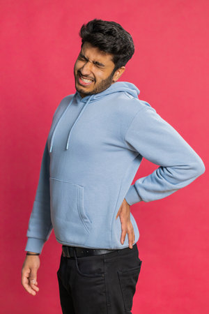 Indian man suffering backache, massaging sore place lower spine, frowning from unbearable spasm torn...