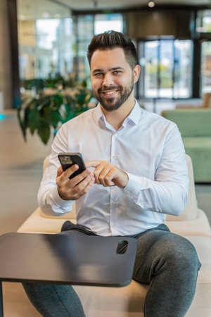 Young smiling Caucasian businessman using smartphone typing text messages, reading email, browsing...