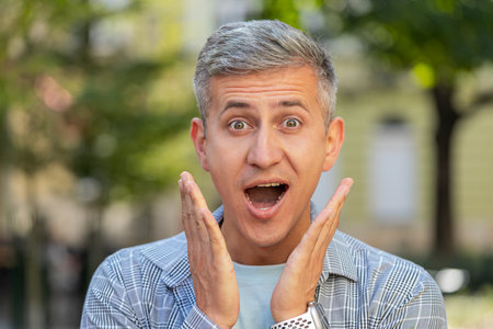 Oh my God, wow. Gray-haired Caucasian man looking surprised at camera with big open eyes, shocked by sudden victory, game winning, lottery goal achievement, good news outdoors. Guy male on city streetの写真素材