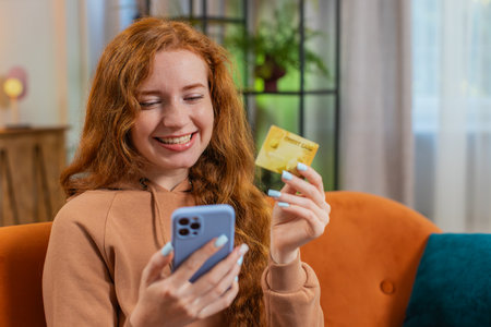 Happy young woman using credit bank card and smartphone while transferring money, purchases online...