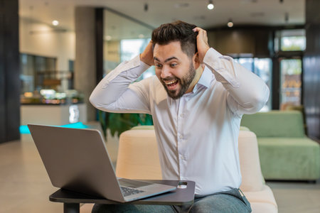 Caucasian bearded businessman working on laptop shocked by sudden victory, game winning lottery goal...