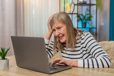 Mature woman experiences system crash error virus on laptop at home. Caucasian grandmother looks...