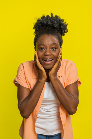Oh my God, Wow. Excited amazed winner African American woman looking at camera with big eyes shocked by sudden victory celebrating success achievement good news. Surprised girl on yellow backgroundの写真素材
