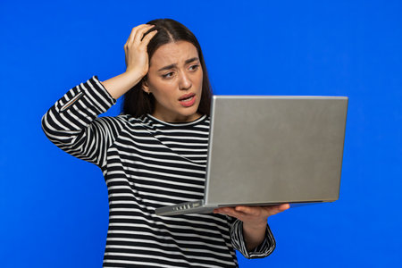 Displeased woman in striped blouse use laptop notebook typing browsing working, loses becoming surprised sudden lottery results bad news fortune loss game fail computer virus. Girl on blue backgroundの写真素材