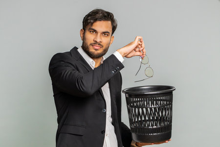 Indian businessman taking off throwing out glasses into bin after medical vision laser treatment therapy surgery looking smiling at camera, heal, cure. Arabian man isolated on studio gray backgroundの写真素材