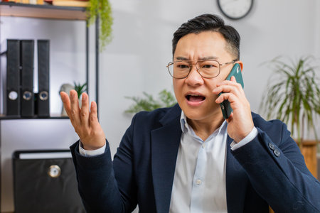 Conflict Quarrel Negotiation. Angry businessman CEO making smartphone online conversation call at office. Upset mad freelancer man talking colleague after analyzing financial report mistake problemの写真素材