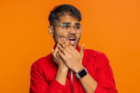 Dental problems. Indian Hindu man touching cheek, closing eyes with expression of terrible suffer from painful toothache, sensitive teeth, cavities. Arabian guy isolated on orange background indoorsの写真素材