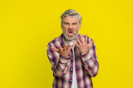 Upset frustrated annoyed Caucasian middle-aged man raising hands in indignant expression, quarreling, asking reason of conflict, why such stubborn. Adult mature guy isolated on yellow backgroundの写真素材