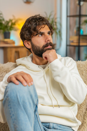 Sad lonely man sits at home room looks pensive thinks over life concerns or unrequited love suffers from unfair situation. Indian alone guy problem, break up, depressed feeling bad annoyed burnout.の写真素材