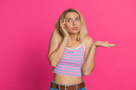 I dont know what to say. Confused Caucasian young woman feeling embarrassed about ambiguous question, having doubts, no answer, idea, being clueless uncertain. Blonde girl isolated on pink backgroundの写真素材
