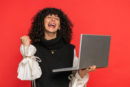 Happy excited Caucasian woman typing on laptop, working on project, enjoying results, winning lottery game celebrating success, online shopping victory good email news. Pretty girl on red backgroundの写真素材