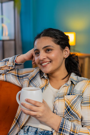 Young woman drinking coffee, looking thoughtfully out window, immersed in deep reflections. Girl experiencing solitude, calm cozy atmosphere of peaceful, quiet home morning momentの写真素材