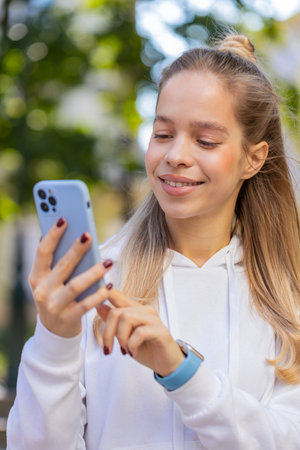 Happy smiling woman using smartphone typing text messages browsing internet social media web app working chatting online outdoor. Young teenager girl tourist standing in urban city street. Verticalの写真素材