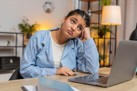 Sad Indian woman looks pensive thinks over life concerns or unrequited love, suffers from unfair situation. Problem, break up, depressed feeling bad, burnout. Girl at home office at table. Lifestyle.の写真素材