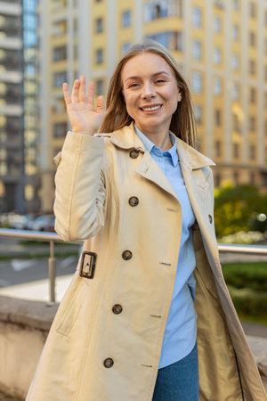 Cheerful mature woman smiling friendly at camera, waving hands gesturing invitation hello, hi, greeting, goodbye, welcoming with hospitable expression outdoors. Happy girl on downtown city street.の写真素材