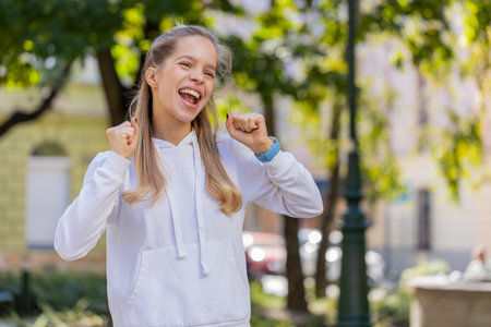 Caucasian young woman looking surprised, shocked by sudden victory, game winning, lottery goal achievement good news, successful interview outdoors. Teenager girl female clenching fists on city streetの写真素材