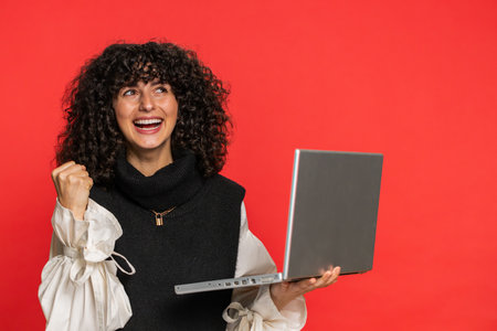 Happy excited Caucasian woman typing on laptop, working on project, enjoying results, winning lottery game celebrating success, online shopping victory good email news. Pretty girl on red backgroundの写真素材