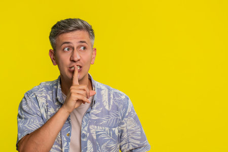 Middle-aged man placing finger on lips with serious focused expression, making silence gesture to ask for quiet and calm. Young guy expressing concentration and request isolated on yellow backgroundの写真素材