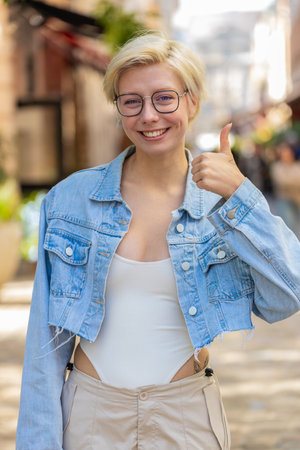 Like. Happy woman shows thumbs up agrees with something or gives positive reply recommends advertisement likes good idea feedback, celebrating success victory. Blonde girl on urban city street.の写真素材