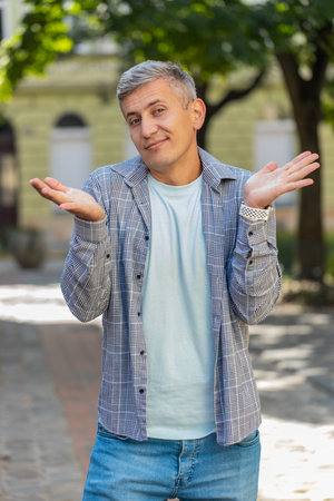 I dont know what to say. Confused man feeling embarrassed about ambiguous question, having doubts, no idea, being clueless uncertain outdoors. Caucasian adult guy standing in city street. Verticalの写真素材