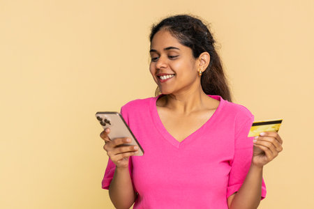 Woman holds credit card, carefully focused on smartphone, making online purchase. Demonstrates...