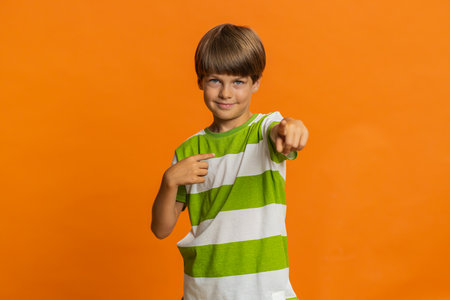 I choose you. Happy young preteen child boy kid pointing finger forward to camera, choosing lucky game winner, indicating to awesome you, promotion. Smiling little children on orange backgroundの写真素材