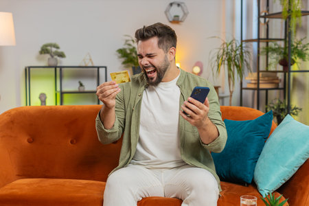 Angry stressed man trying to pay online shopping with smartphone blocked credit card. Annoyed Caucasian brunette guy buying bank refuse problem unsuccessful payment lack of money balance at home.の写真素材