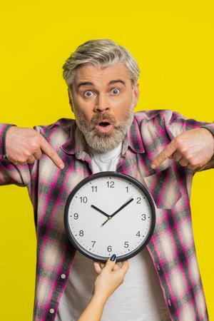 Mature man lifts office clock with worried face highlighting close call and racing anxiety. Guy...