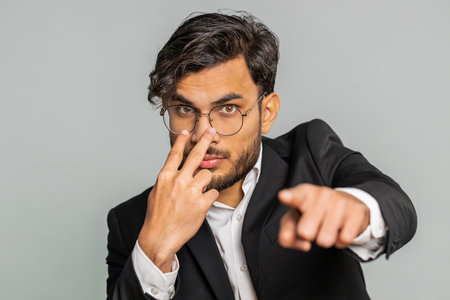 Confident attentive businessman pointing at his eyes and camera show I am watching you gesture spying on someone. Handsome disappointed Indian man isolated on gray studio backgroundの写真素材