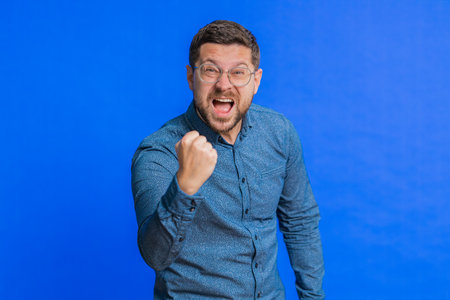 Displeased young man gesturing hands with irritation and displeasure, blaming scolding for failure, asking why this happened. Brunette attractive guy isolated on blue studio backgroundの写真素材