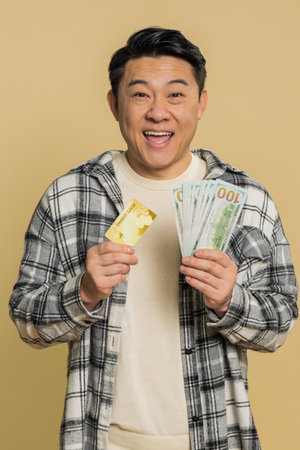 Happy Asian middle-aged man showing plastic credit bank card and money dollar cash for purchases...