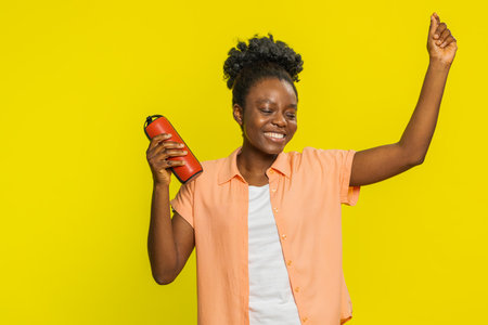African American woman holds red portable speaker, moving energetically to the rhythm of music with ease. Black girl isolated on yellow background showing joy relaxation while enjoying favorite tunesの写真素材