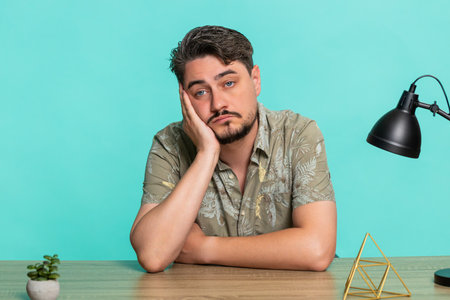 Middle-aged man sits at table with blank stare, head supported by hand, showing emotional burnout,...