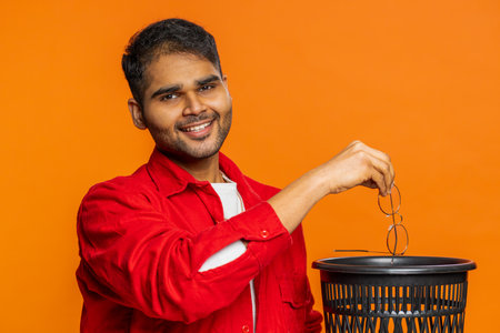 Man taking off throwing out glasses into bin after medical vision laser treatment therapy surgery looking smiling at camera, heal, cure. Guy isolated on studio orange backgroundの写真素材