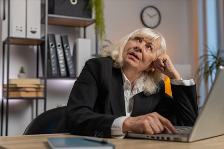 Exhausted tired Caucasian woman freelancer workaholic girl. Bored sleepy elderly businesswoman working on laptop computer yawns, leaning on hand at home office desk.の写真素材