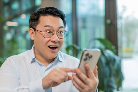 Wow. Happy amazed mature businessman working on smartphone shocked by sudden victory game winning lottery jackpot achievement good career news. Excited man in shirt is sitting in office hotel lobby.の写真素材