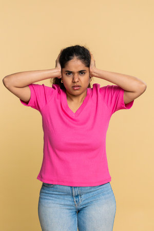 Woman quickly covers ears with hands, frowning strongly, clearly disturbed by loud noise. Shows discomfort, unwillingness to listen, irritation from disturbing sounds around her.の写真素材