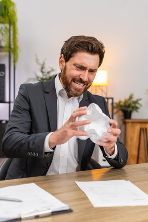 Middle-aged businessman at home office finds errors and crumples report exhales hard and calms. Freelancer guy at table opens new document edits lines fixes text and continues work with focus again.の写真素材