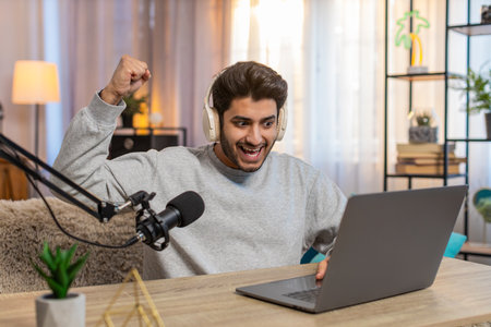 Young Indian man playing online game on laptop actively reacting to games events during live stream,...