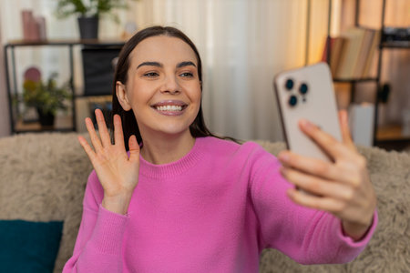 Young woman at home having video call smiling, laughing and actively gesturing while talking to a friend. Caucasian girl on sofa enjoying fun conversation with strong emotion and positive energyの写真素材