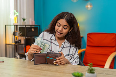 Woman at home counts dollars cash placing bills into wallet feeling secure financial satisfaction...