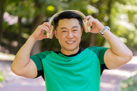 Happy young Japanese man put on wireless modern headphones earphones. Runner jogger guy sport male...