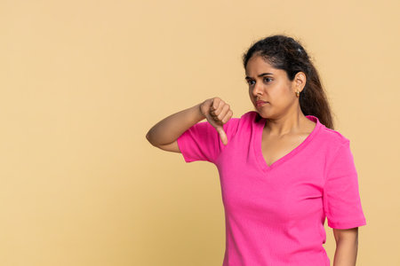 Indian woman lightly shakes head with clear disappointment, lowers shoulders shows thumbs down. Girl...