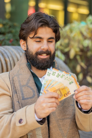 Successful rich young man holding and waving euro bill money fan on downtown city street. Happy adult guy winning online lottery game offers a cash loan for purchases calculating budgetの写真素材