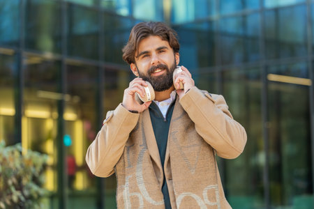 Joyful relaxed overjoyed business man listening favorite energetic disco rock n roll music outdoors. Adult guy taking off wireless headphones looking at camera smiling on downtown city street.の写真素材
